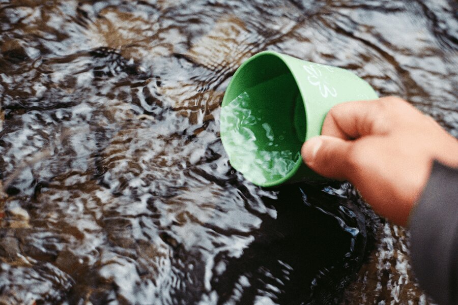 Nabranie vody v potoku do zeleného kelímka. Zdroj: https://www.pexels.com/cs-cz/foto/66090/