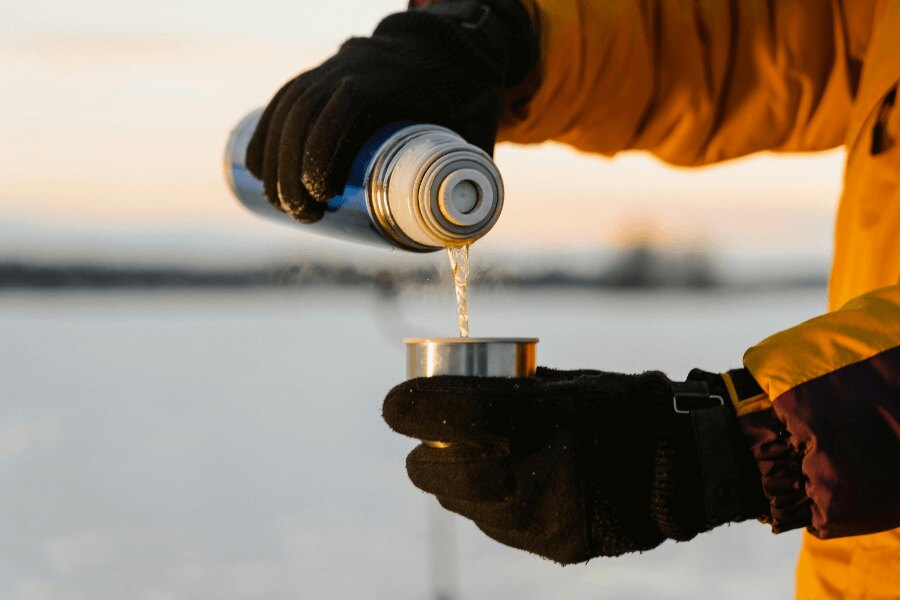 Nalievanie nápoja z nehrdzavejúcej termosky v zimných rukaviciach. Zdroj: https://www.pexels.com/cs-cz/foto/ruce-voda-liti-termoska-6831063/