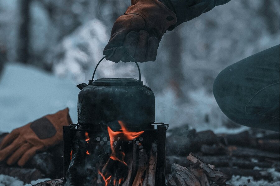 Varenie v outdoorovej kanvici na drevnom ohrievači. Zdroj: https://www.pexels.com/cs-cz/foto/ruka-v-rukavici-drzi-konvici-nad-ohnem-v-zime-13611509/